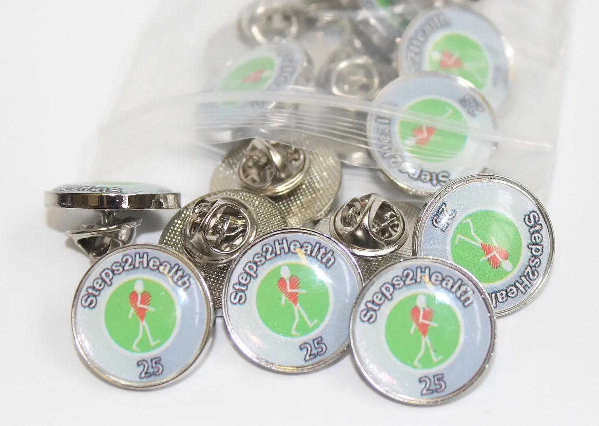 Bag of green Steps2Health 25 round printed pin badges